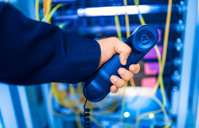 Close-up of a hand holding a telephone receiver in a server room emphasizing technology.