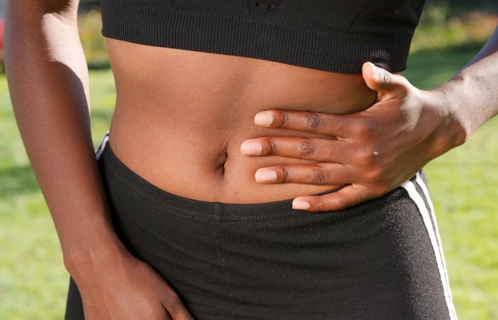 Close-up of a person holding their abdomen, indicating stomach discomfort, outdoors.