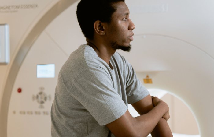 A man sits before a CT scanner, preparing for a medical examination, conveying a sense of anticipation.