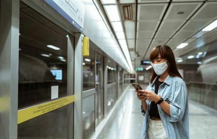 Asian woman in denim jacket using smartphone at subway station.