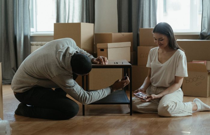 A couple assembling a coffee table amid stacked moving boxes in their new home.