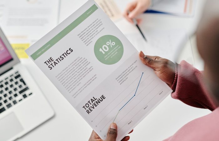 Hands holding a statistical report during a business meeting. Includes revenue graphs and analysis.