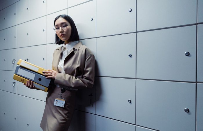 Businesswoman in office attire standing with documents, appearing poised in a modern office setting.